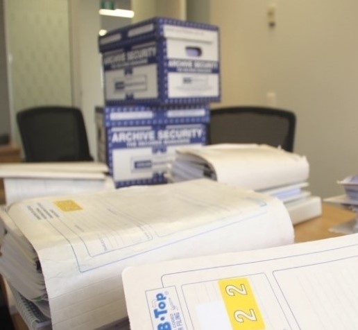 Image of large files on a table with boxes of files in the background.